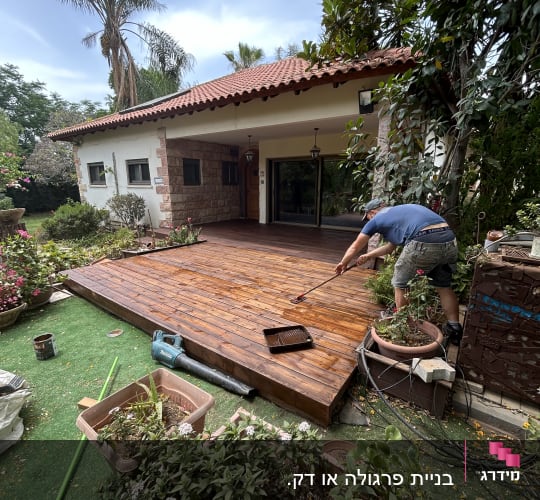 אדם צובע דק עץ בגינה עם מברשת צבע